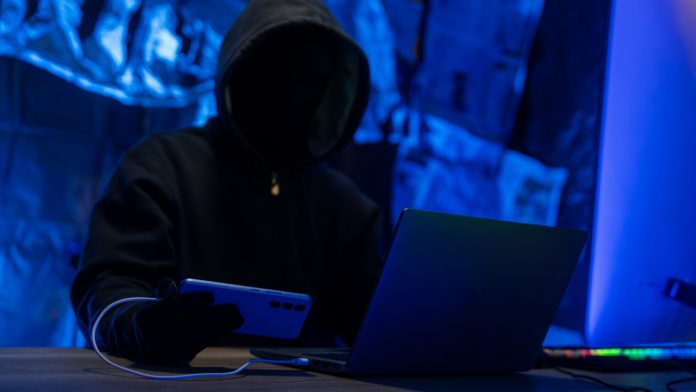 Hacker Using Laptop and Smartphone in a Dimly Lit Room
